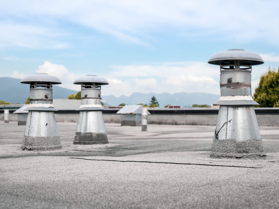 Flat roof vents on building with 2 ply SBS or modified bitumen roofing system. Group of metal ventilators such as: bathrooms and laundry exhaust and plumbing stack vent. Selective focus.